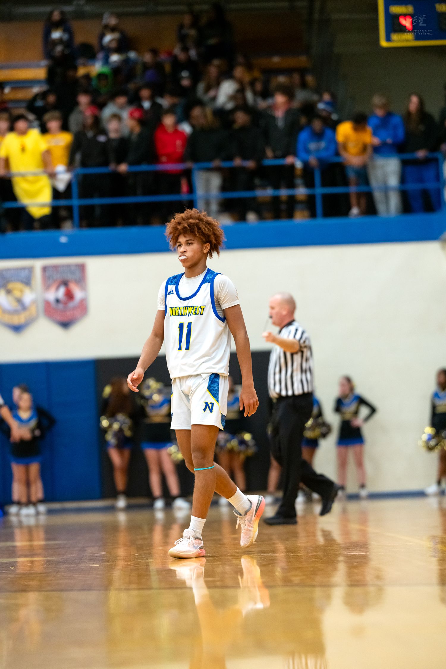 Northwest basketball player #11 walks on court during a high school game in a packed gymnasium.