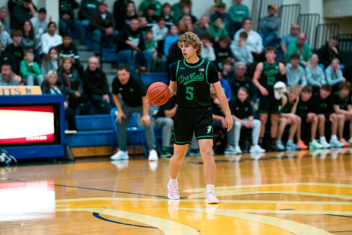 Player in green number 5 jersey dribbles basketball at center court during crowded game.