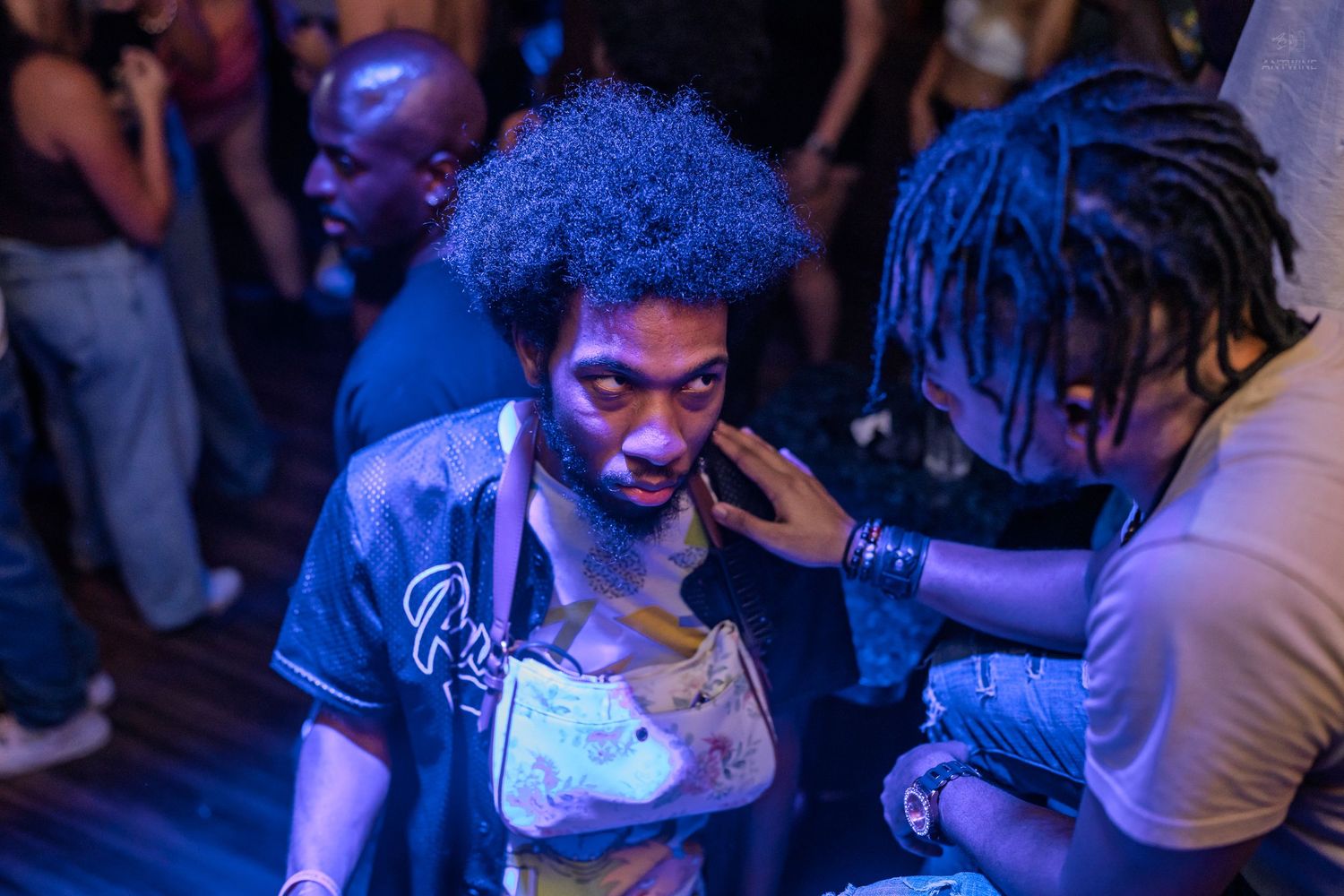 Young man with blue afro hair enjoying a nightclub party under colorful atmospheric lighting.