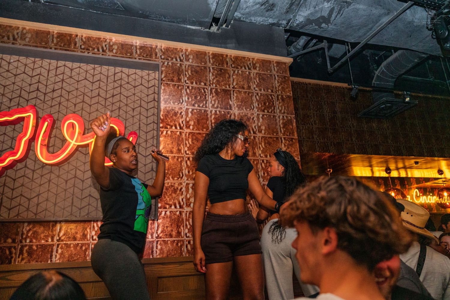 Two women dancing on stage near a red neon sign at a Cincinnati nightclub.