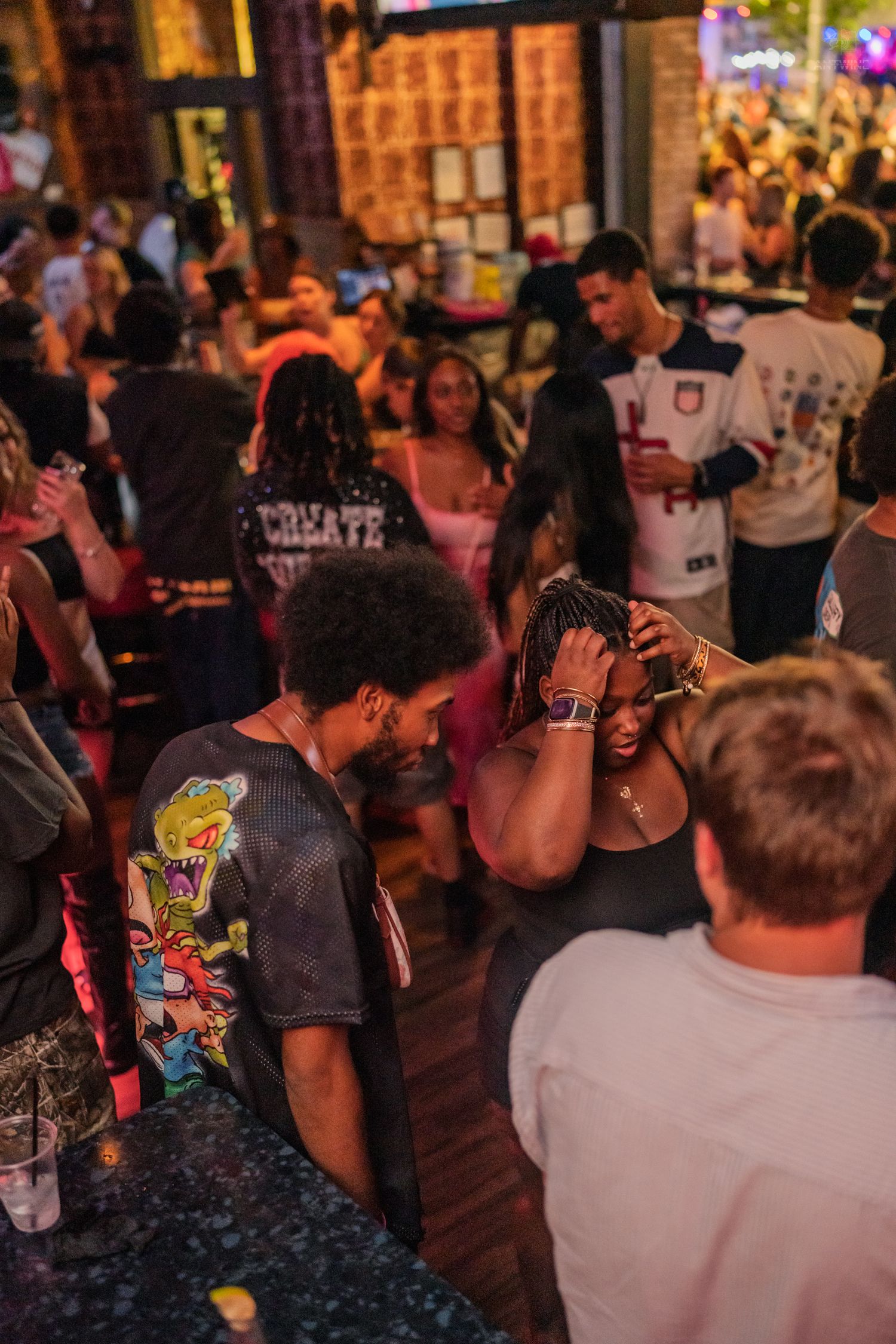 Young people mingling and dancing at a lively indoor bar party with warm ambient lighting.