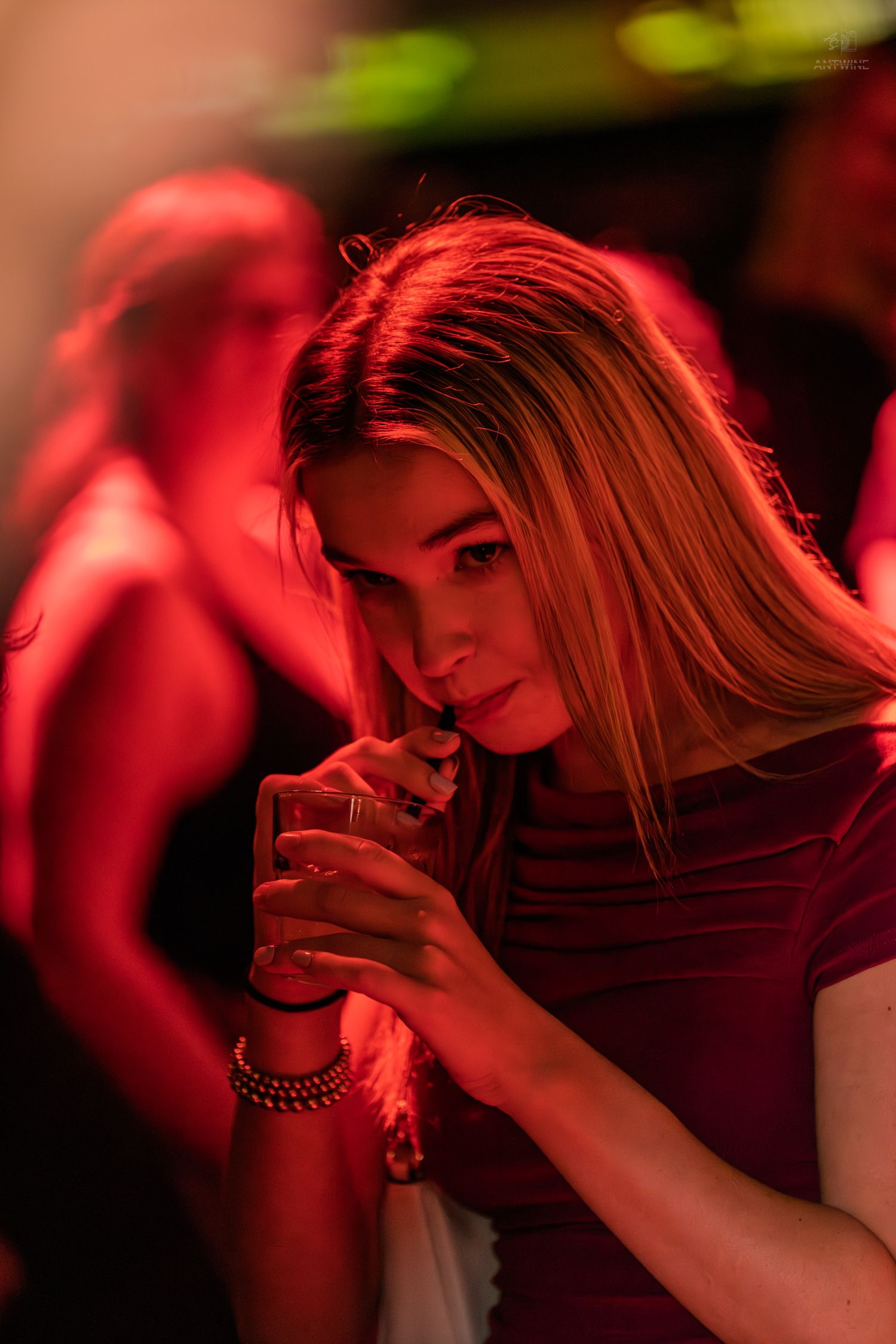 Young woman sipping a drink bathed in red neon light at a nightclub.