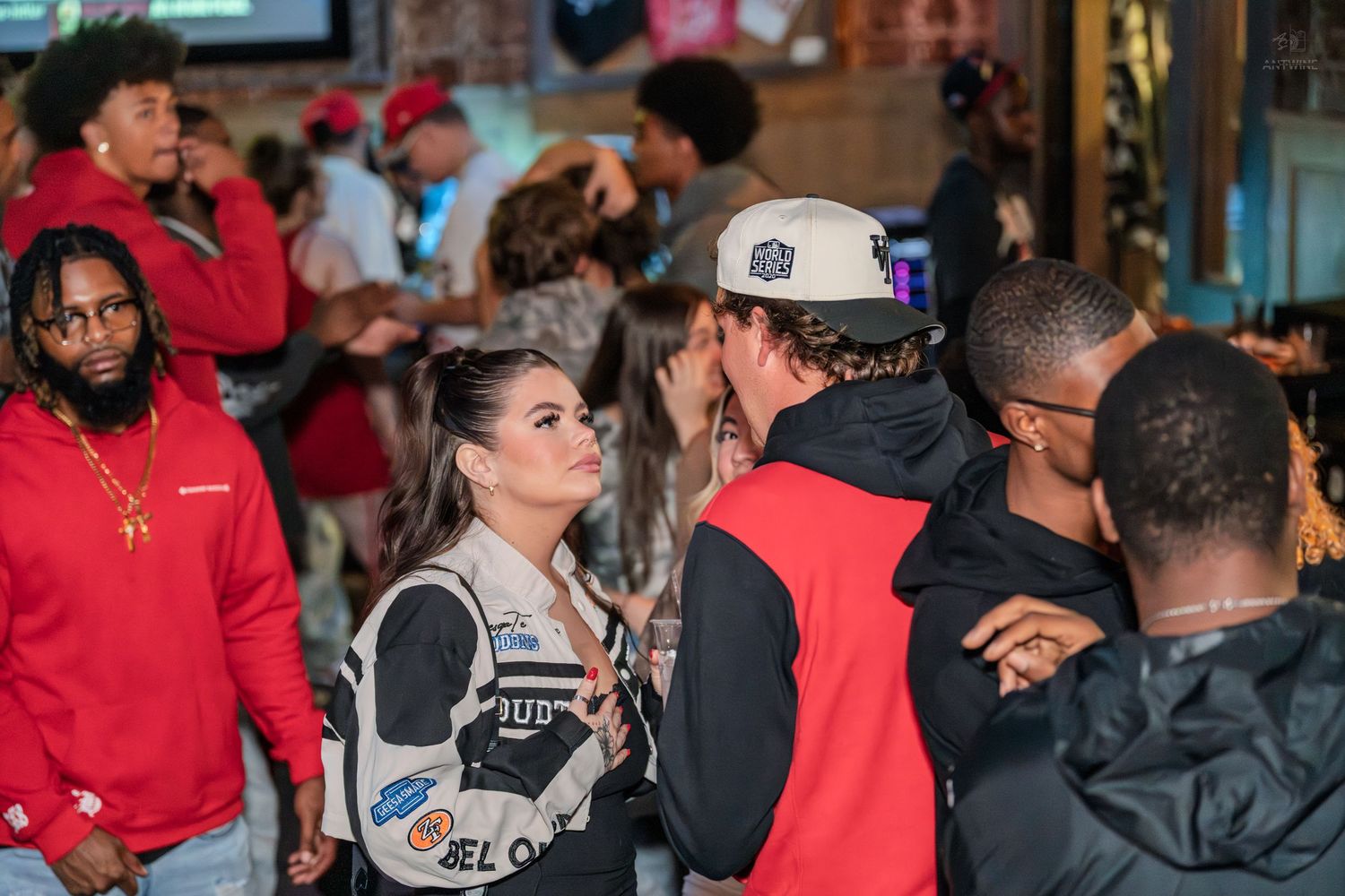 Diverse group of young adults socializing at a lively indoor bar or nightclub event.