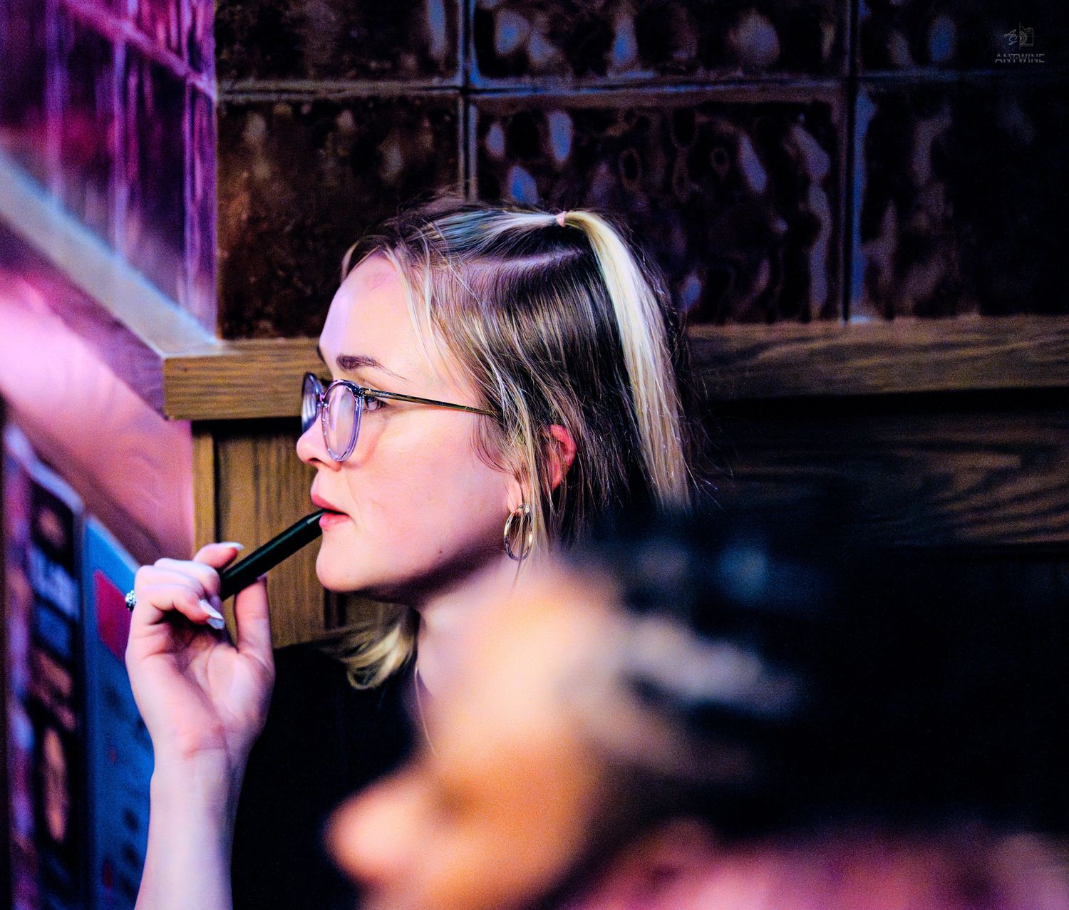 Black and white candid photo of a woman with a floral shoulder tattoo talking on her phone at a bar.