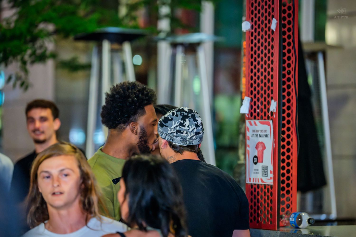 People mingling near red decorative wall at outdoor nighttime social event.