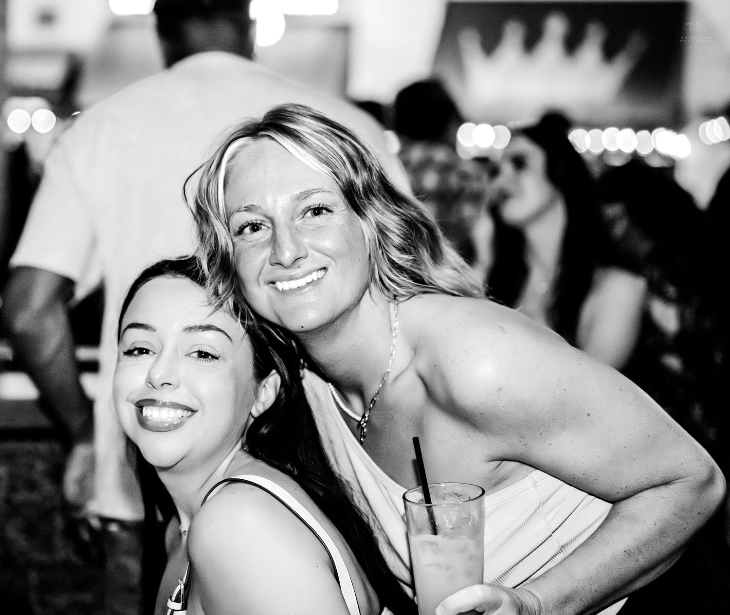 Two young women smiling and posing together in a black and white photo at a bar.