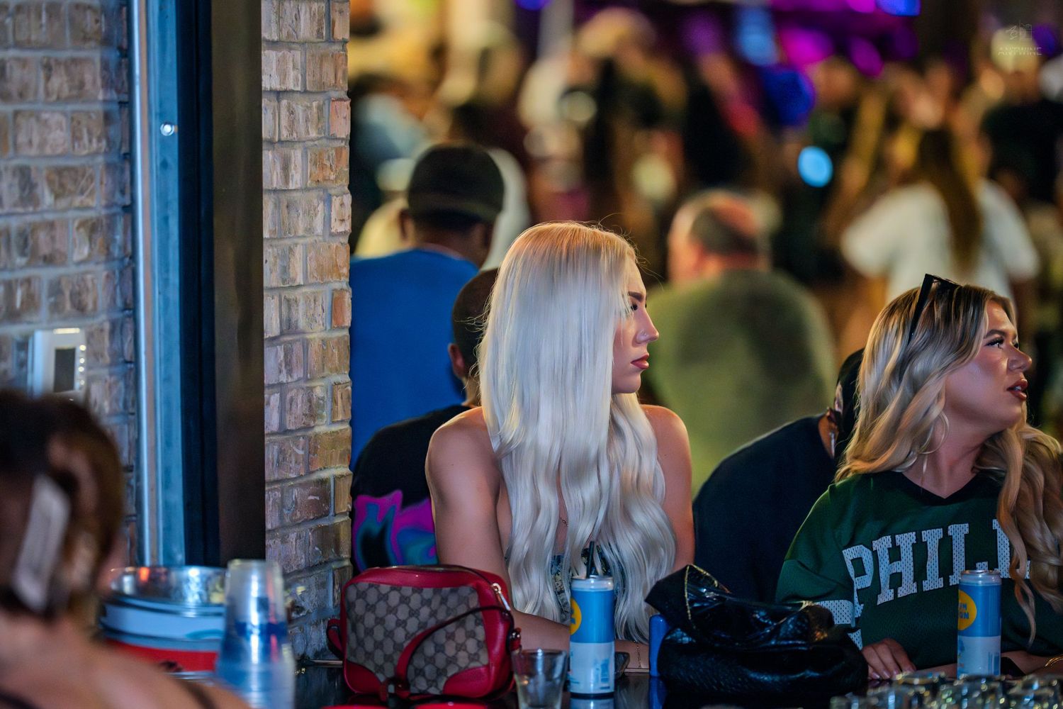 Blonde woman in a crowded bar wearing a Gucci bag at night.