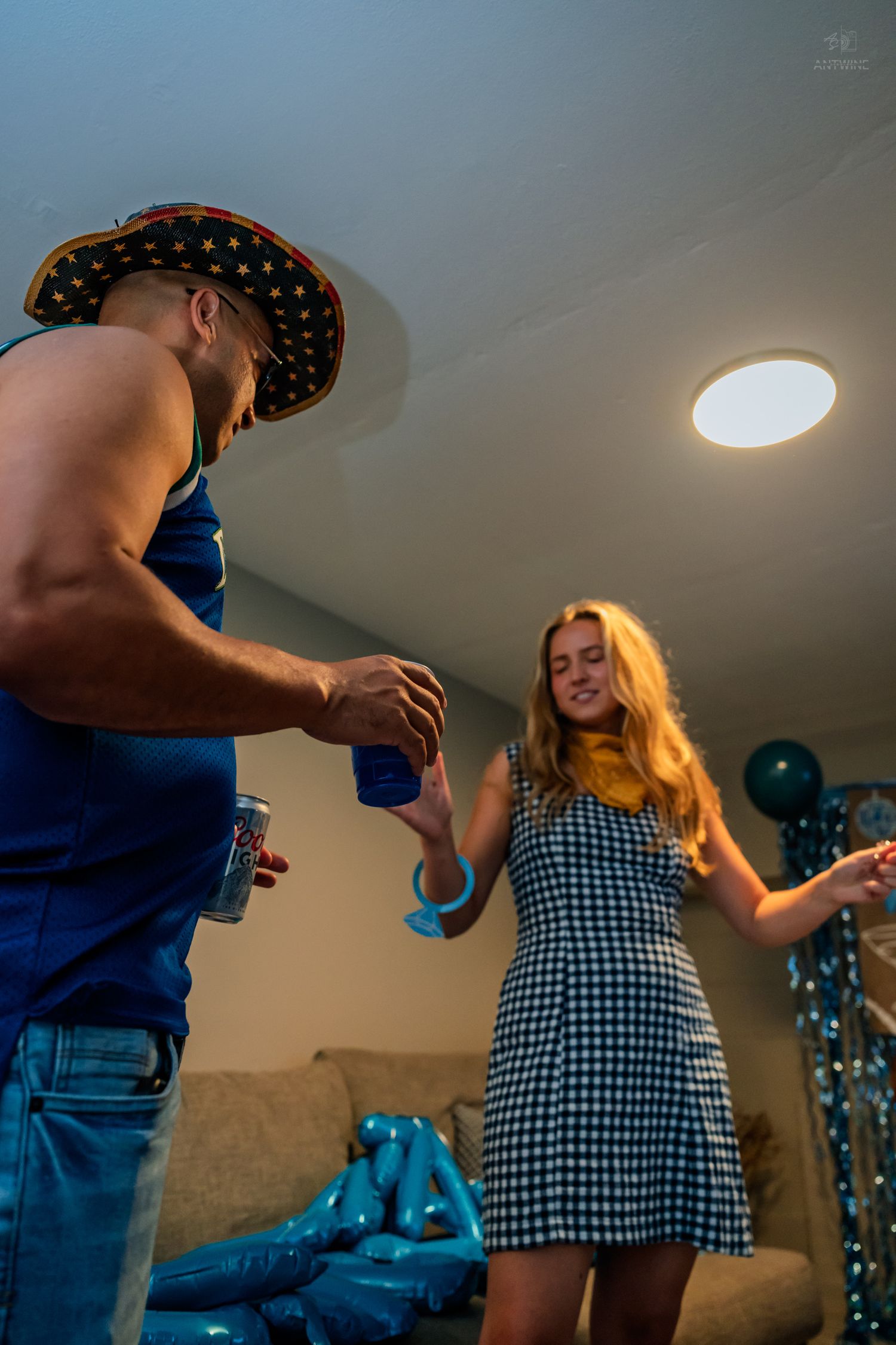 Man in party hat giving wristband to smiling woman in checkered dress at party.