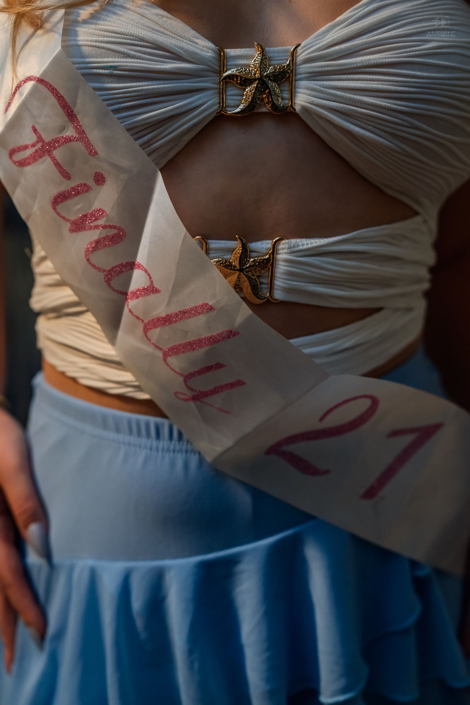 Woman wearing a white 'Finally 21' birthday sash over a silver crop top and blue skirt.
