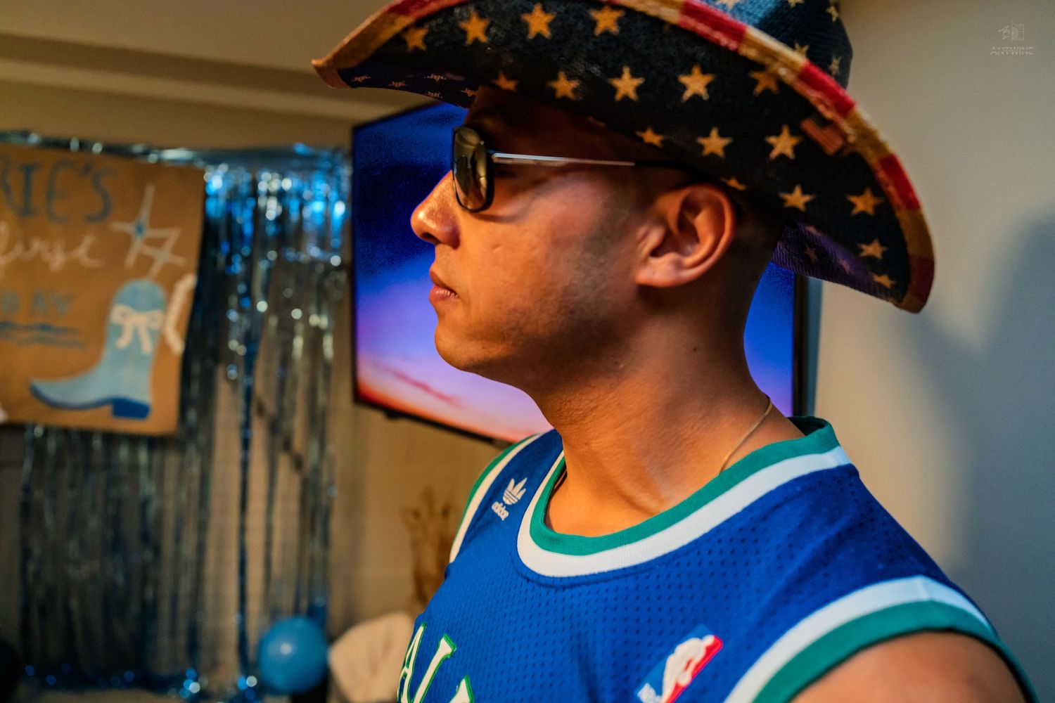 Man wearing a star-spangled cowboy hat and sunglasses at a birthday party with blue decorations.