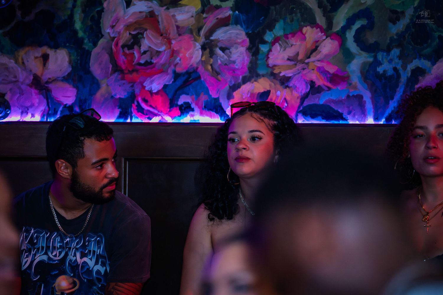 Couple sitting together in a dimly lit nightclub with floral wall art behind them.