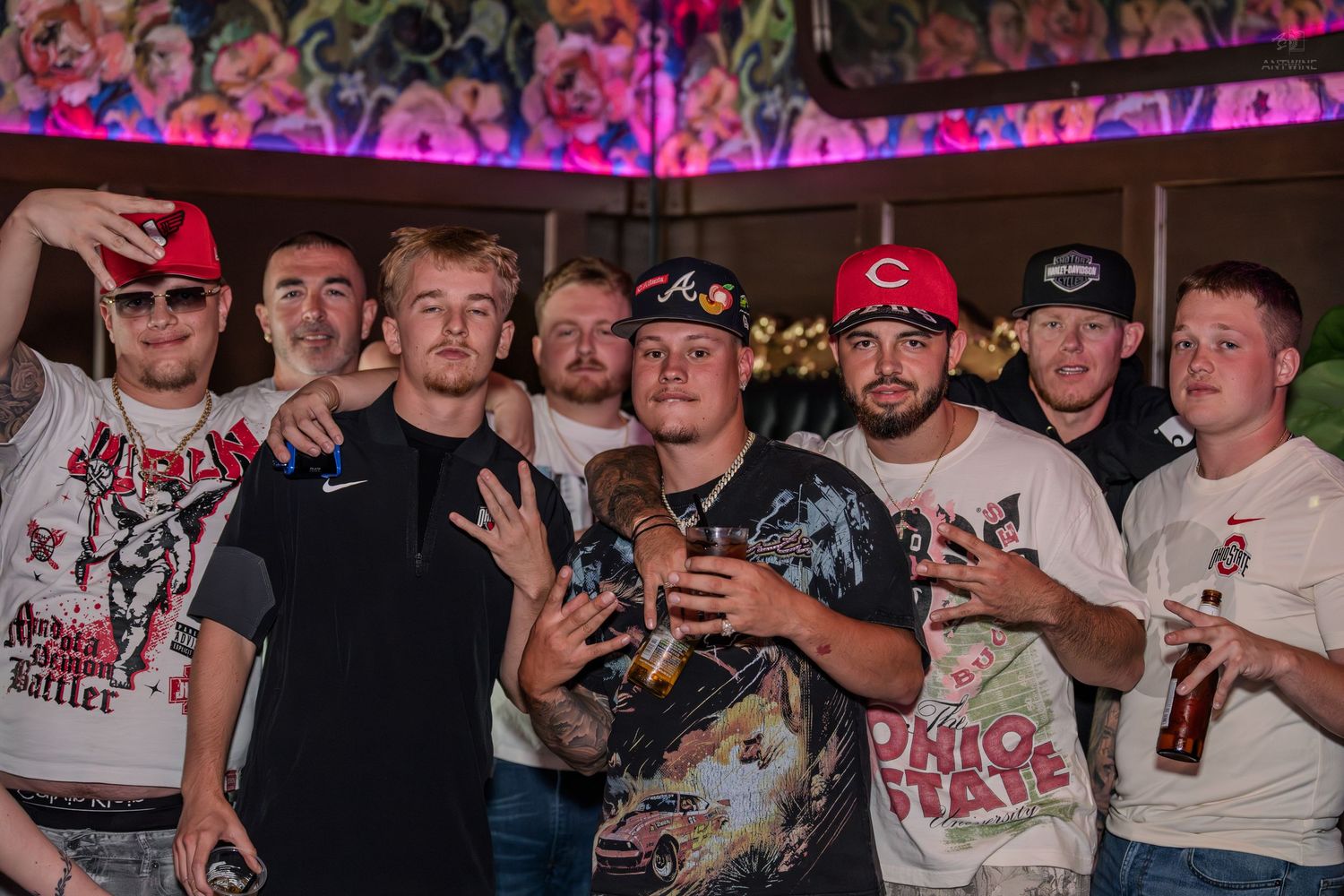 Group of guys posing and making hand gestures at a lively bar nightclub event.