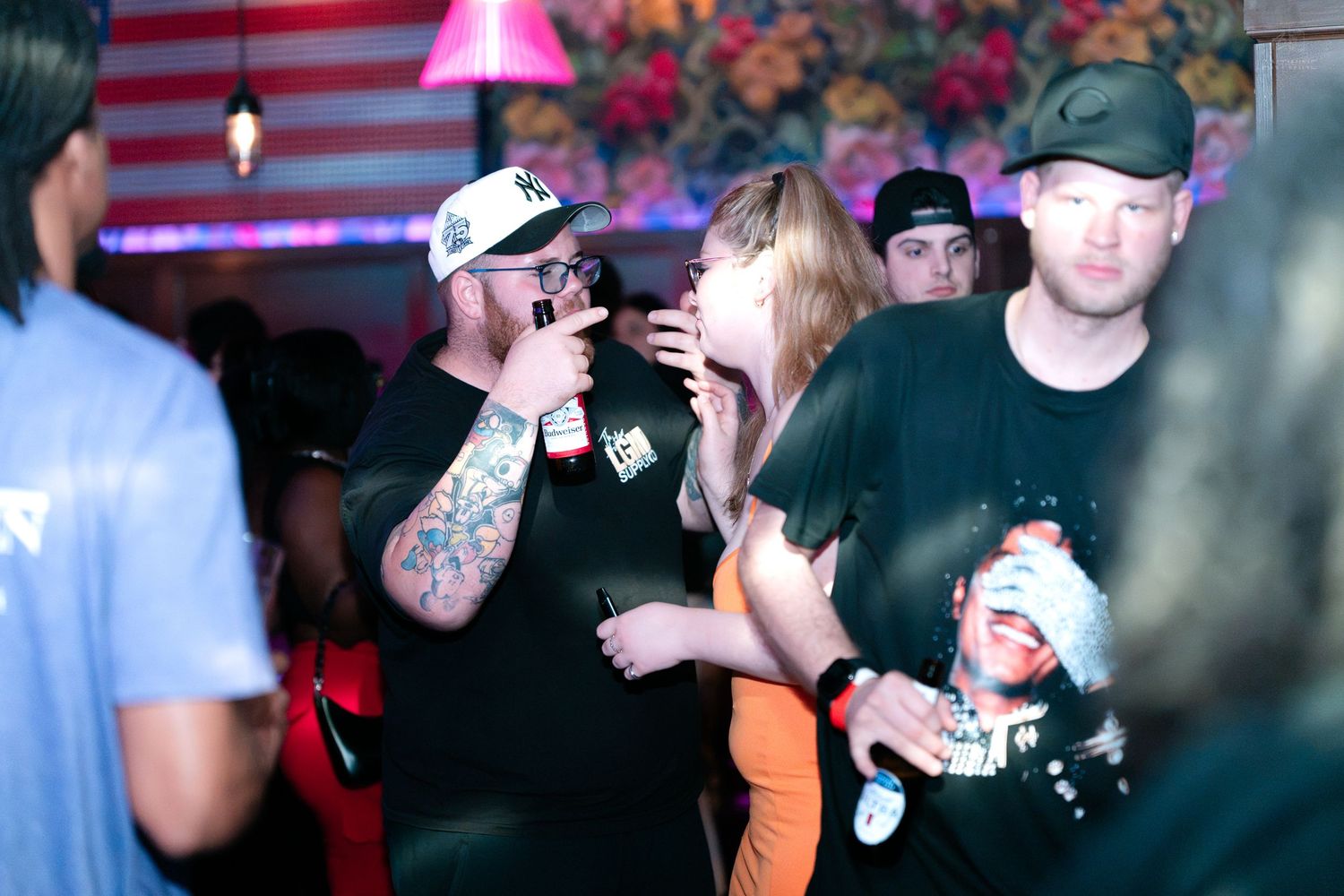 Tattooed man and friends socializing at a lively nightclub with floral wall decor.