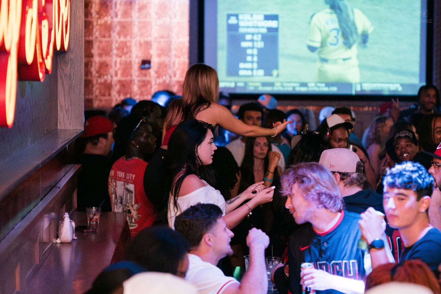 Crowded bar scene with guests cheering and watching sports on a large screen TV.