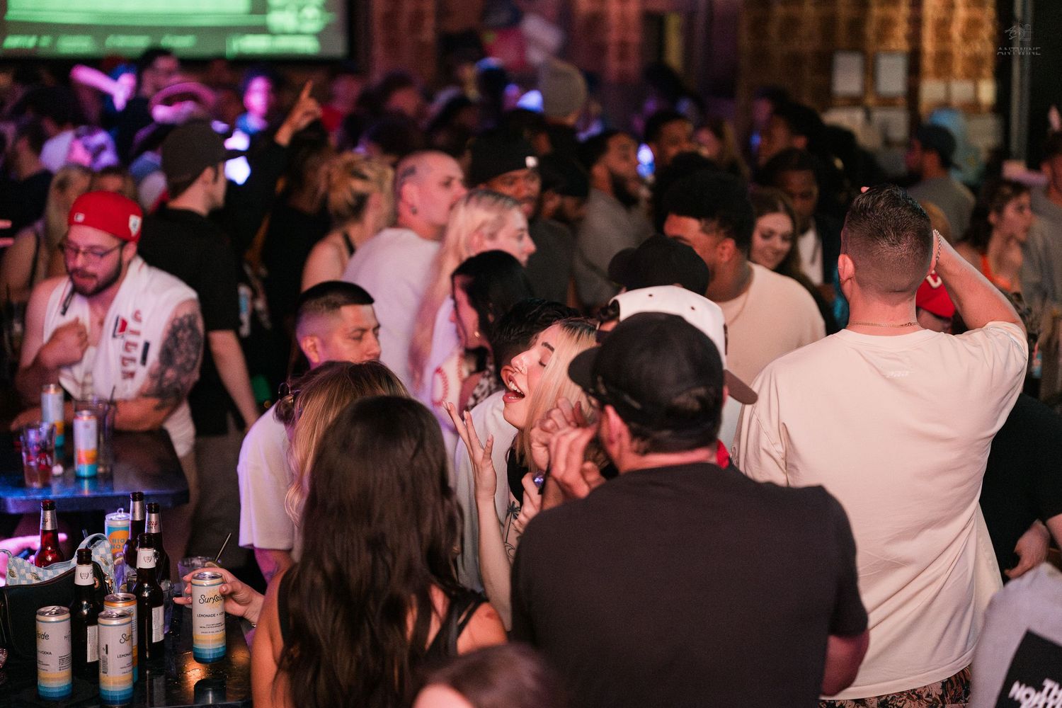 Large crowd of people mingling and dancing at a packed nightclub bar event.