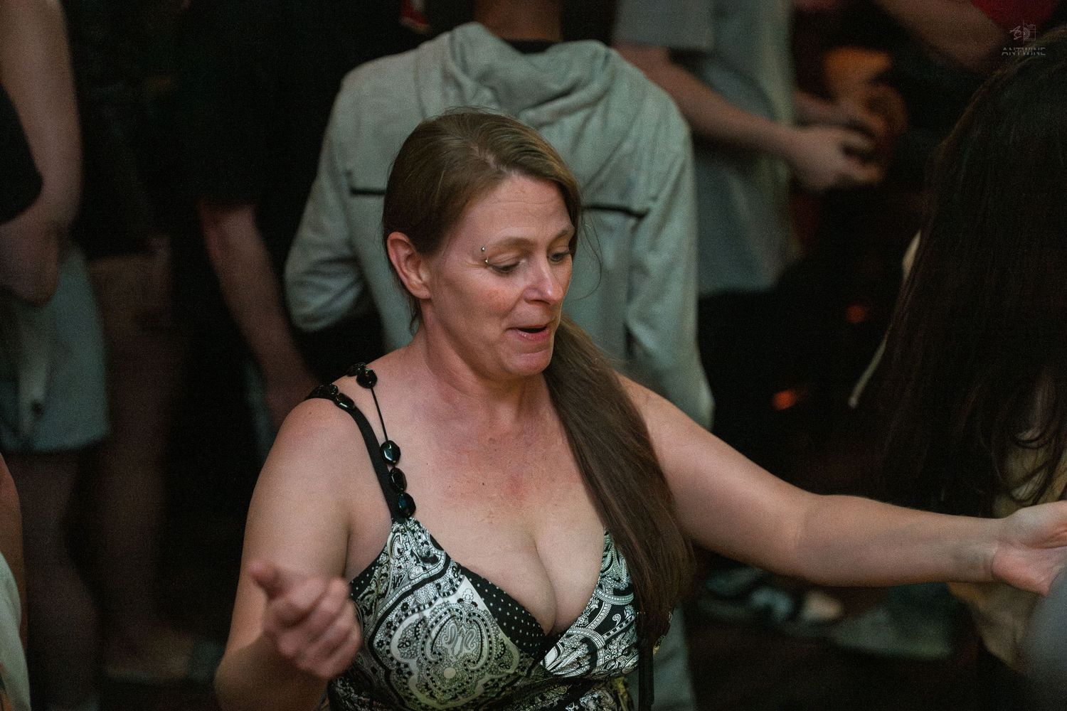 Middle-aged woman in patterned swimsuit top dancing freely at a crowded indoor nightlife event.