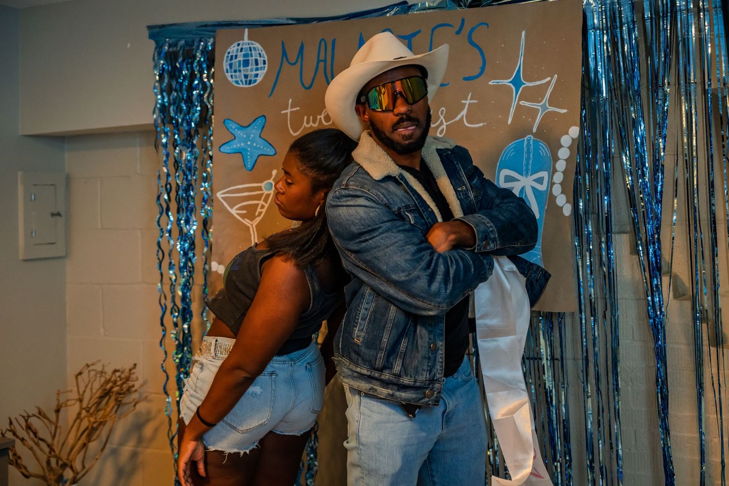 Man and woman posing back-to-back at a blue-decorated 21st birthday party celebration.