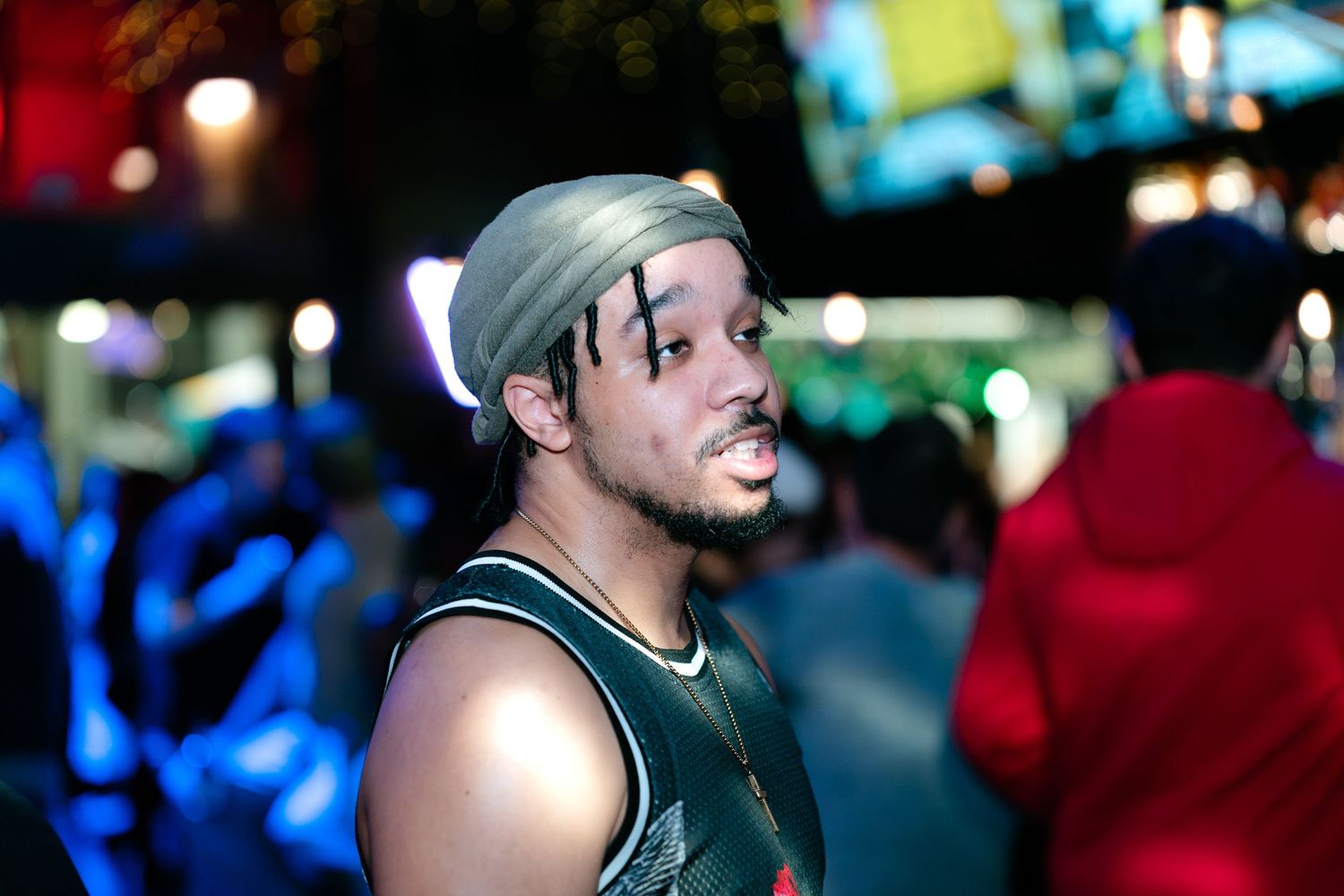 Young man with gold headband and beard poses outdoors at a nighttime street event.