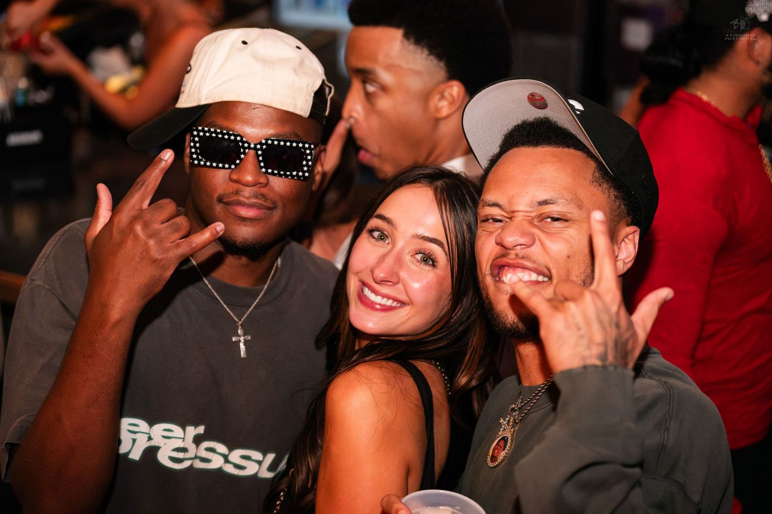 Three friends posing and making fun gestures at a nightclub party.