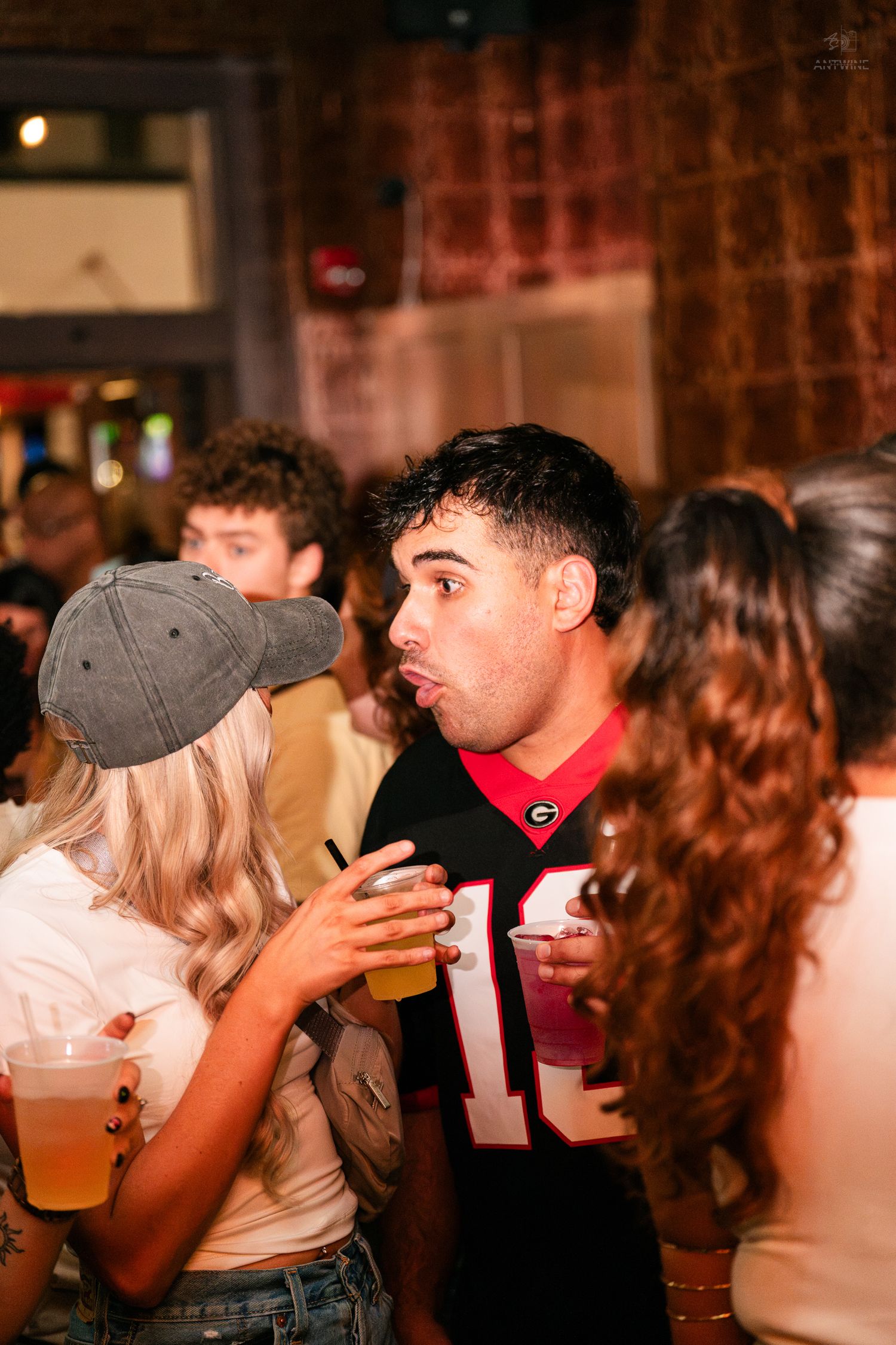 Young man in Georgia Bulldogs jersey making a funny face while holding a drink at a bar.
