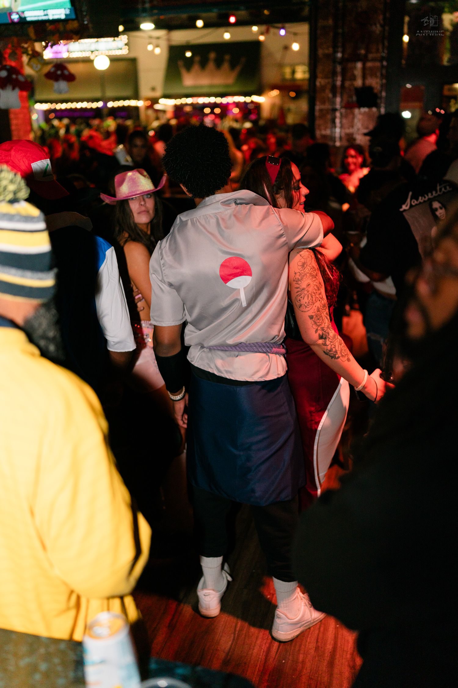 Person in Naruto Uchiha clan costume at a crowded Halloween party on a dance floor.