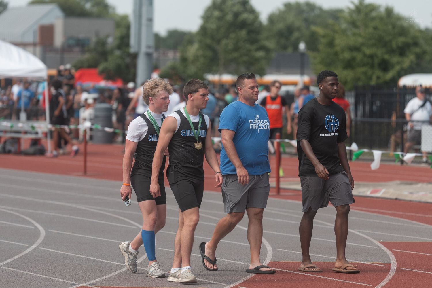 Four track and field athletes walk together on a red track during an outdoor high school competition.