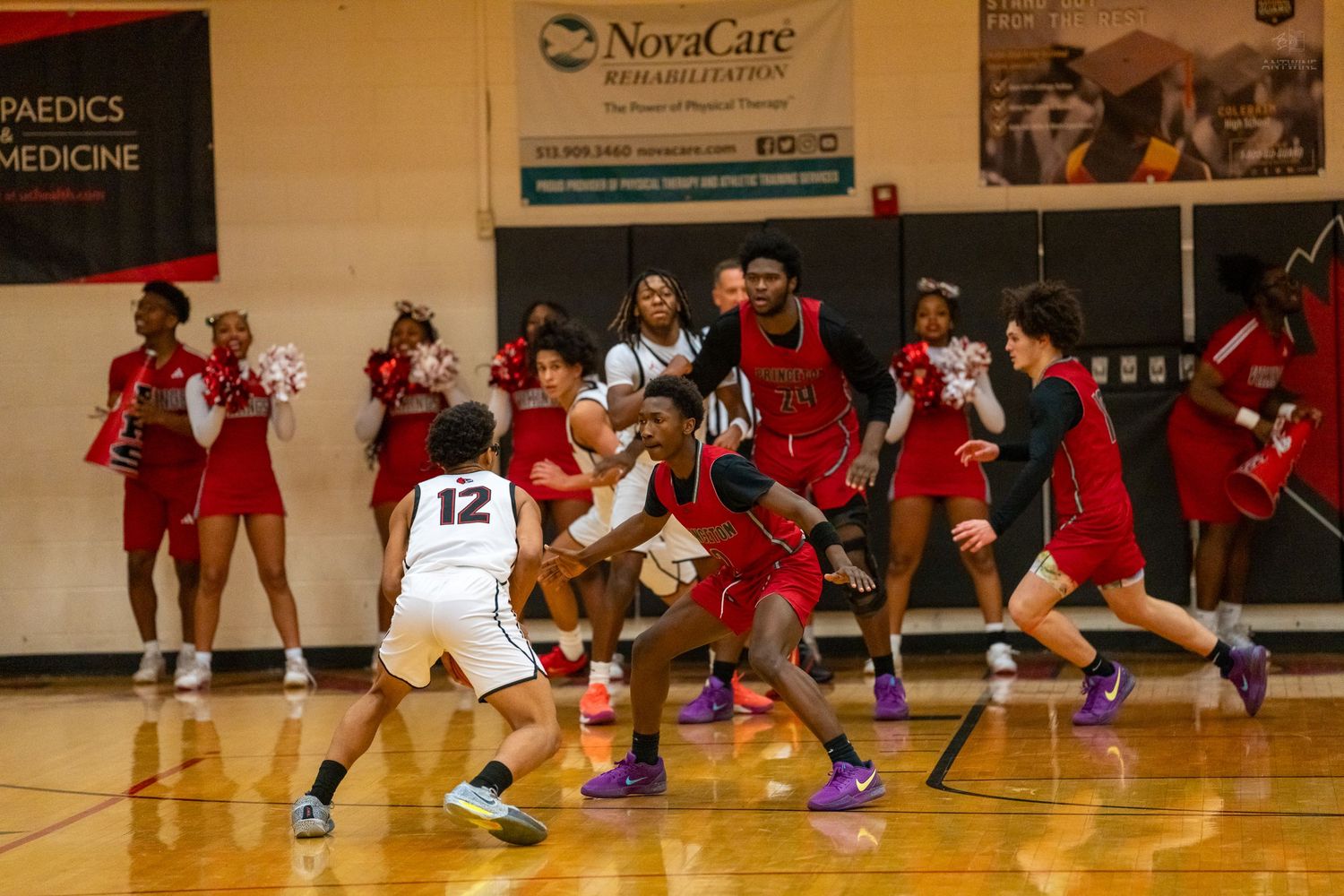 Players scramble for ball near sideline during intense indoor basketball game.