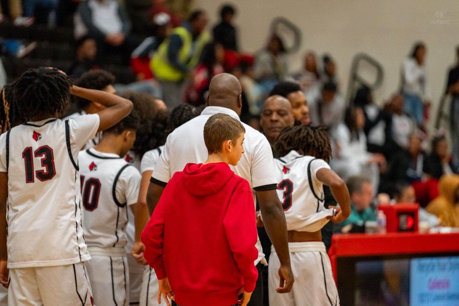 Basketball team huddles with coaches during timeout, players wearing white uniforms with numbers 13, 10, and 3 visible.