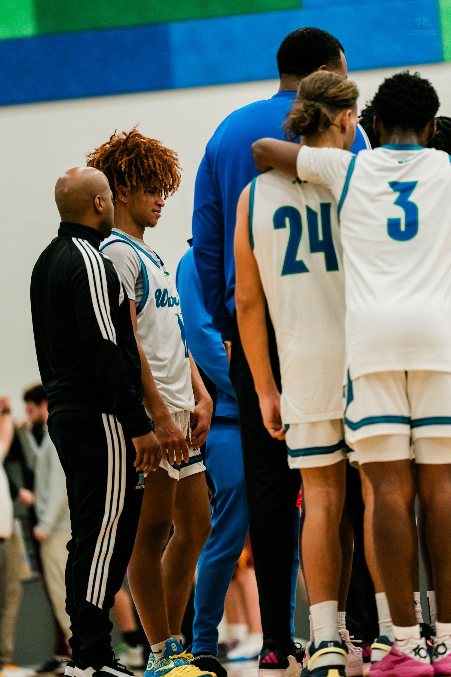 Warriors basketball coach talks with player #11 on the sideline while teammates #24 and #3 stand nearby.