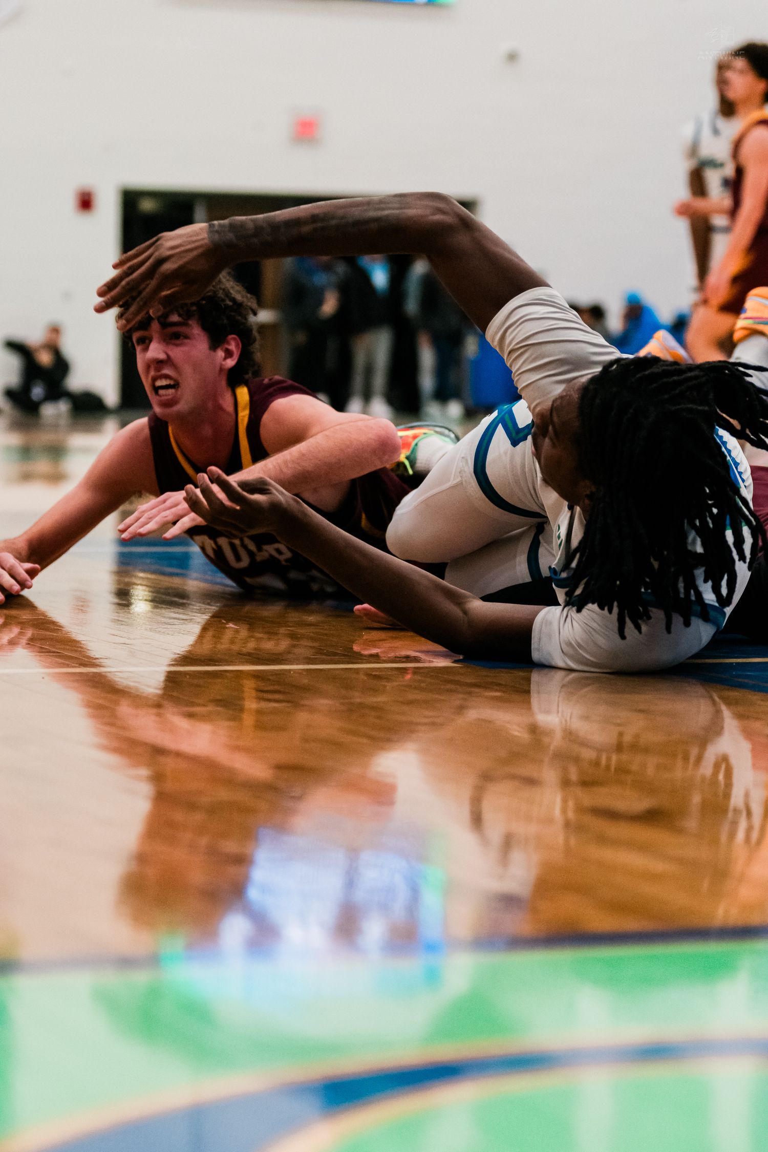 Two basketball players scramble for a loose ball on the hardwood court during an intense high school game.