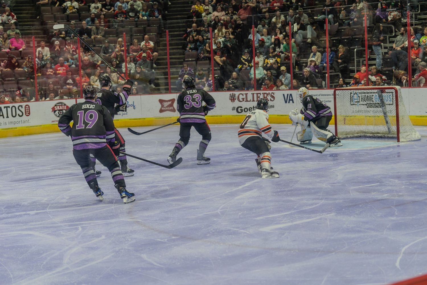 Hockey players in purple jerseys attack the goal during an intense professional ice hockey game.