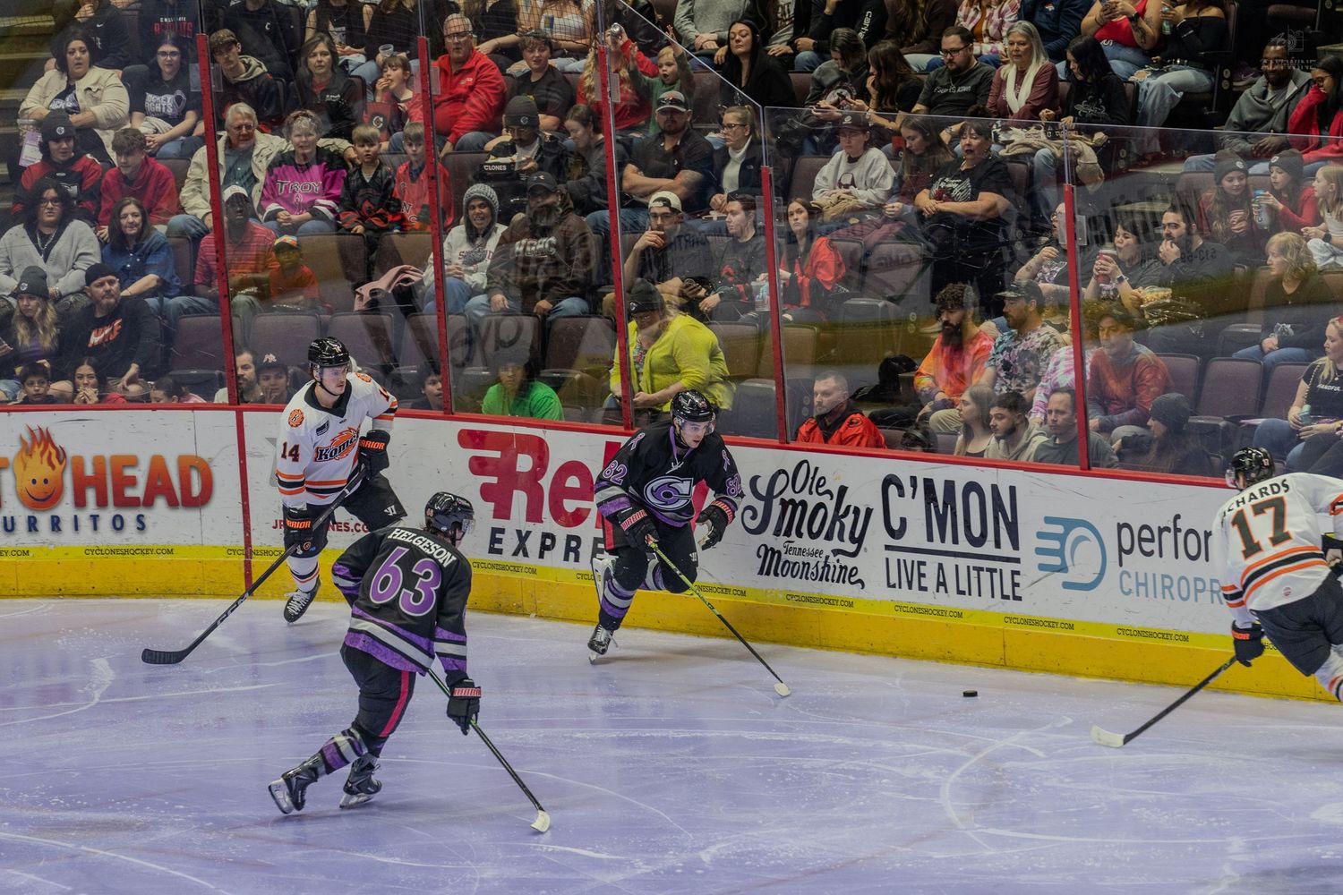 Hockey players skate up ice during a fast-paced professional hockey game in a packed arena.
