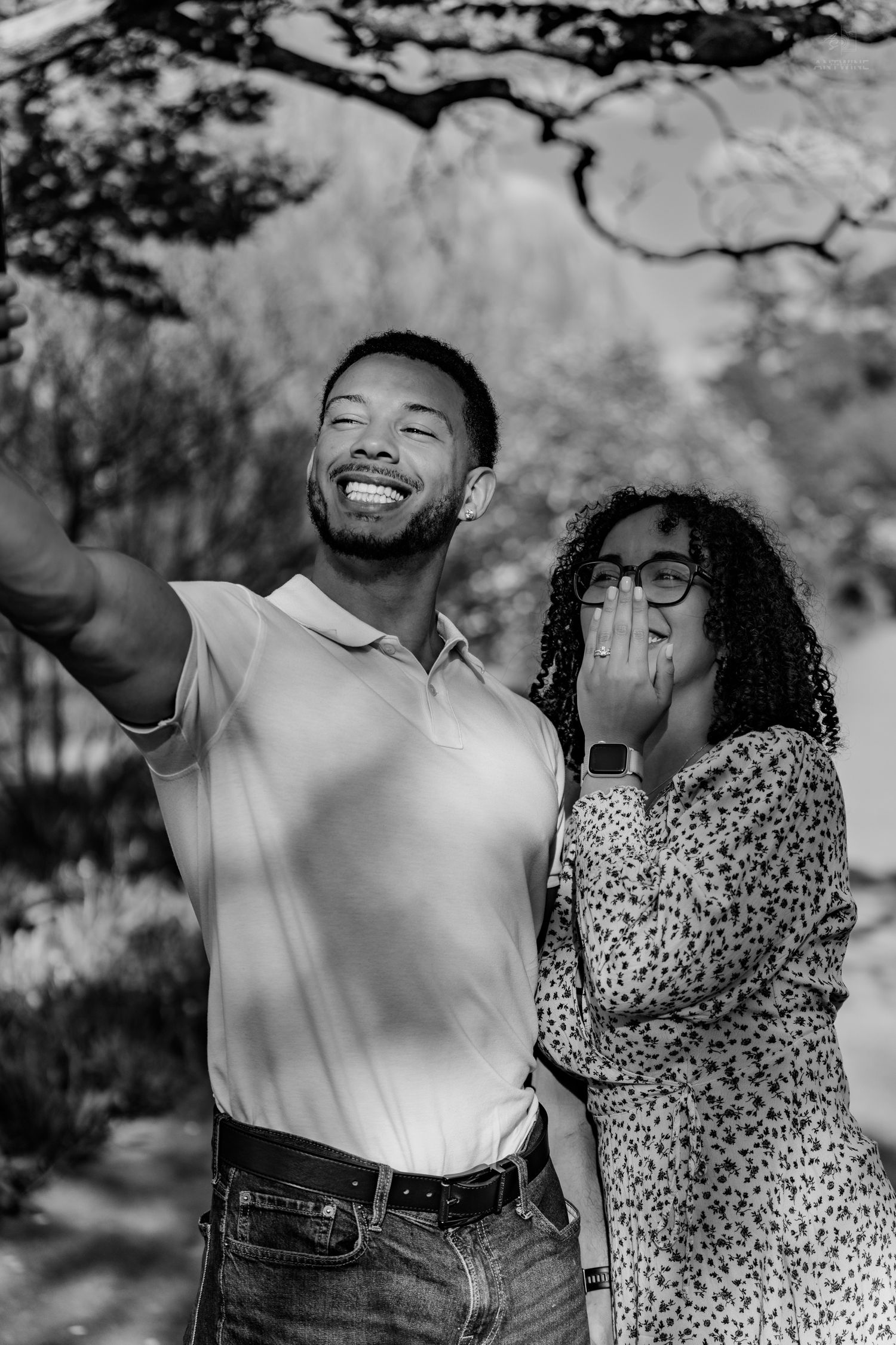 Black and white photo of couple taking a selfie outdoors, woman covering mouth in surprised delight.