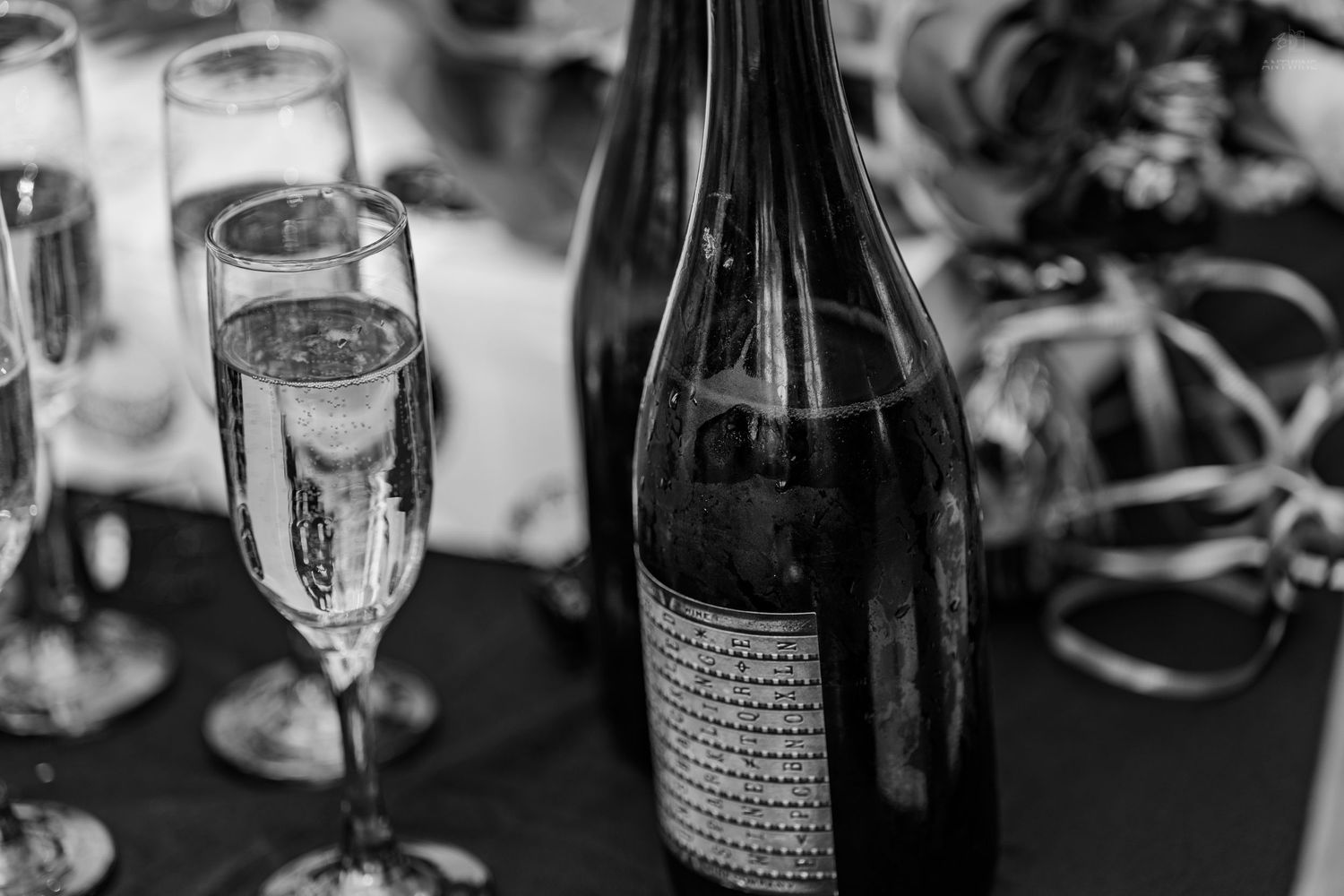 Champagne bottle and two filled flutes on a dark table, black and white photo.