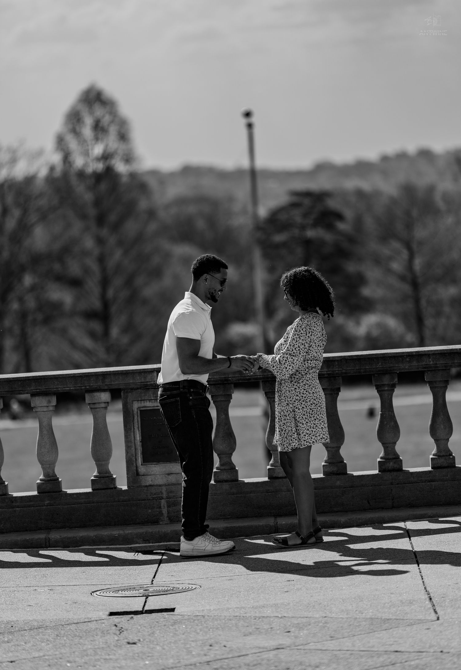 Black and white image of couple sharing a tender moment on a stone terrace in a park.