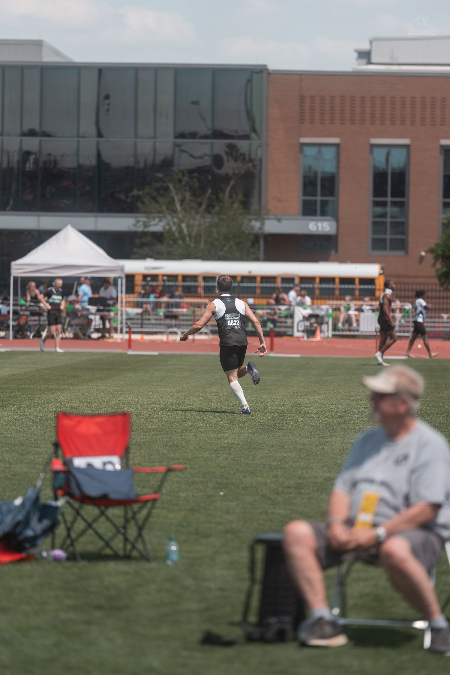 Track athlete in black uniform running on artificial turf field during outdoor athletics competition.