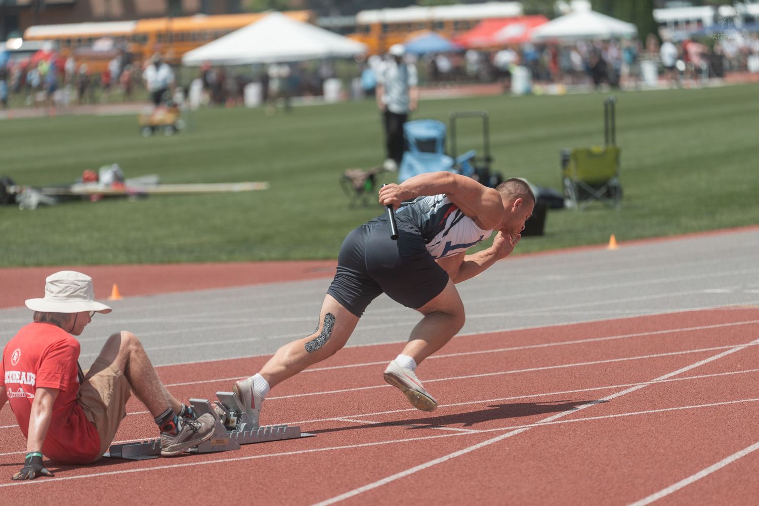 Sprinter exploding off starting blocks at a sunny outdoor track meet at Ohio State University.