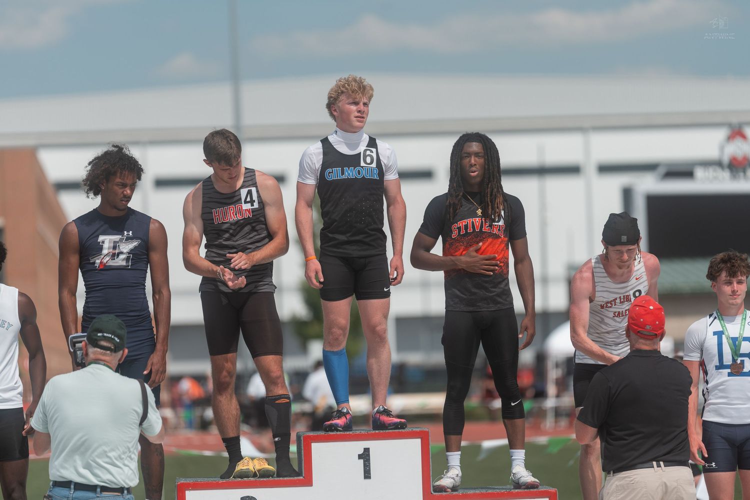 Young male athletes stand on numbered award podium at OHSAA track and field championship meet.