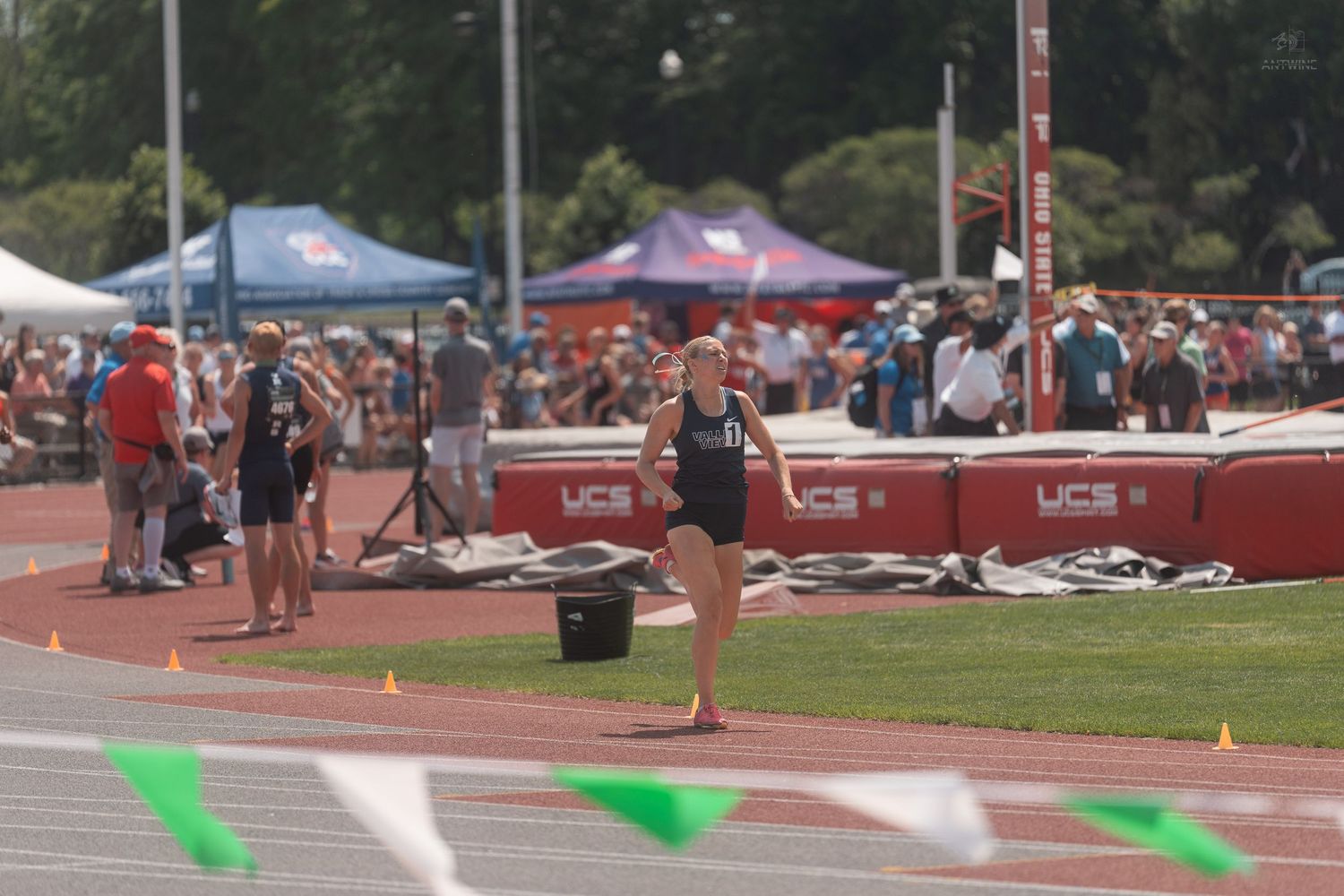 Female athlete competing in track and field event at outdoor stadium with spectators.