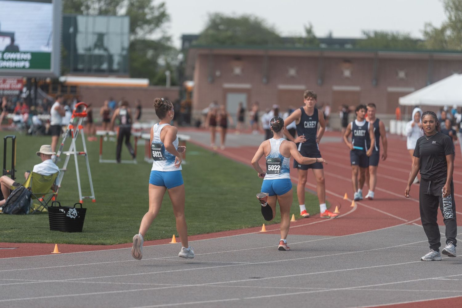 Female runners compete in a track race during an outdoor high school track and field championship meet.