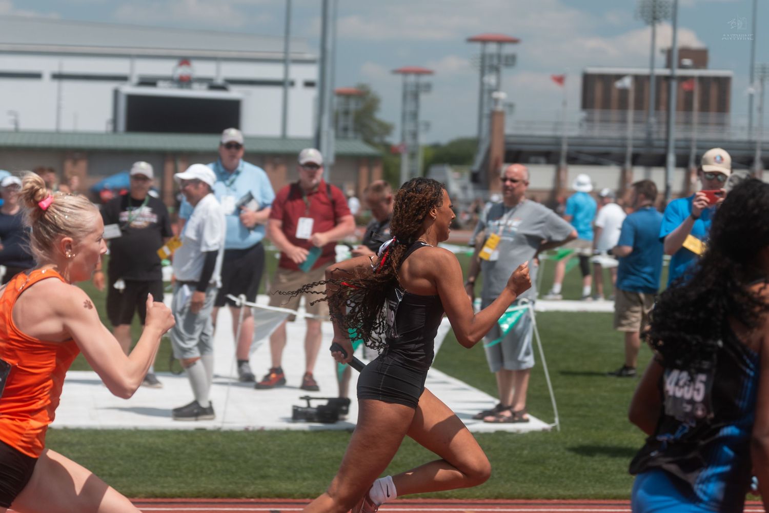 High school girls sprint on a red track at a competitive OHSAA track and field championship meet.