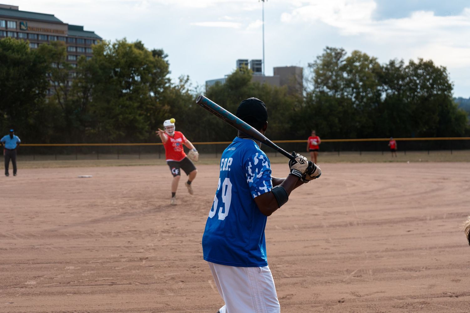 A softball player in a blue number 99 jersey swings a bat on an outdoor dirt field.