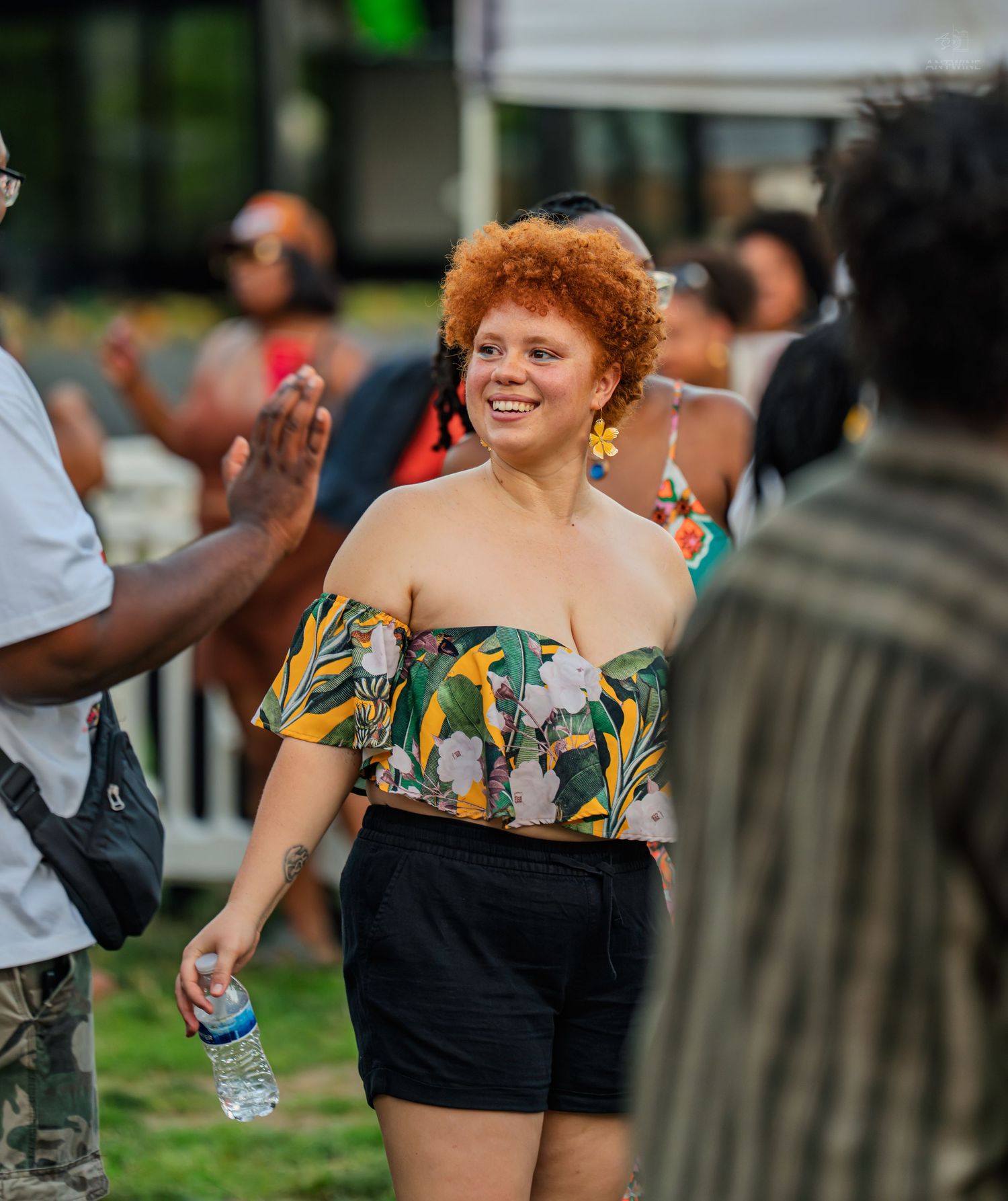 Smiling woman with red curly hair in floral top enjoying an outdoor summer block party event.