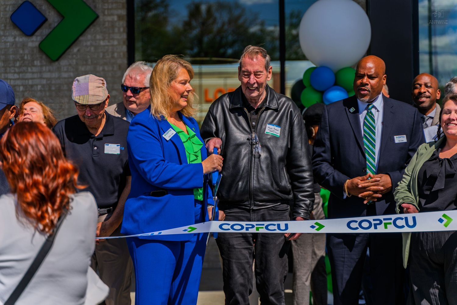 COPFCU officials and guests celebrate a ribbon cutting ceremony outside a new credit union branch.