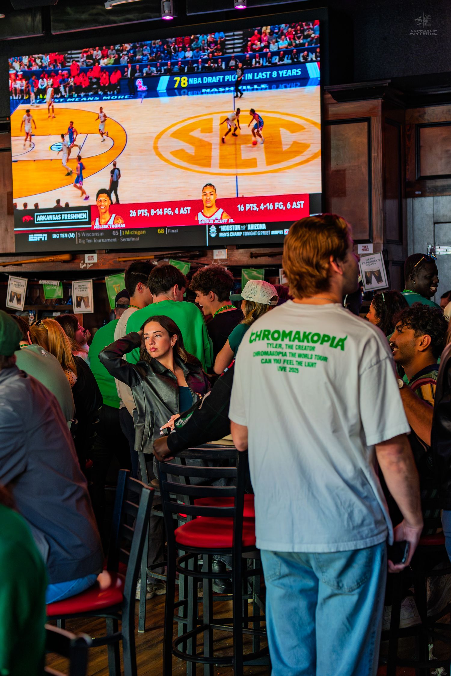 Crowd of college students watching SEC basketball game on large screen TV at a sports bar.