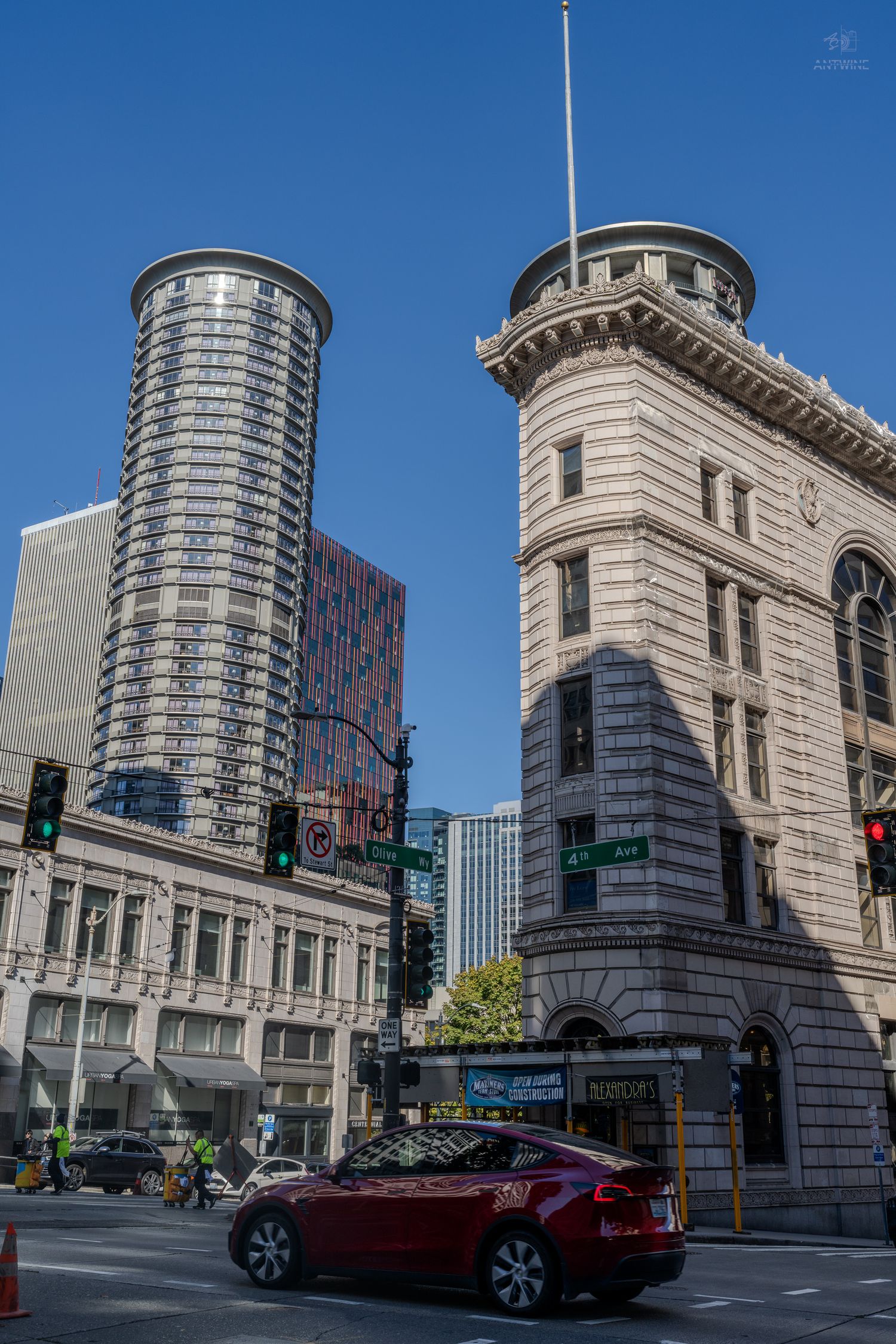 Historic Beaux-Arts building beside a modern cylindrical glass skyscraper at a Seattle downtown intersection.