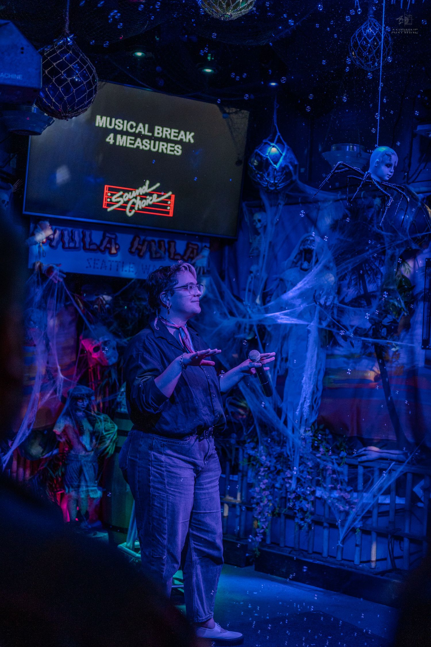 Person performing at a Halloween-themed karaoke bar with a Musical Break 4 Measures sign glowing in blue light.