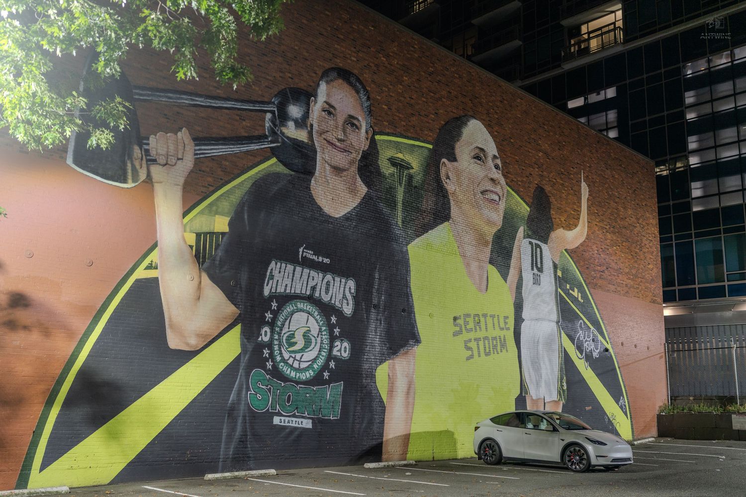 A large mural of two female basketball players, one in a Champions shirt, painted on a building wall at night.