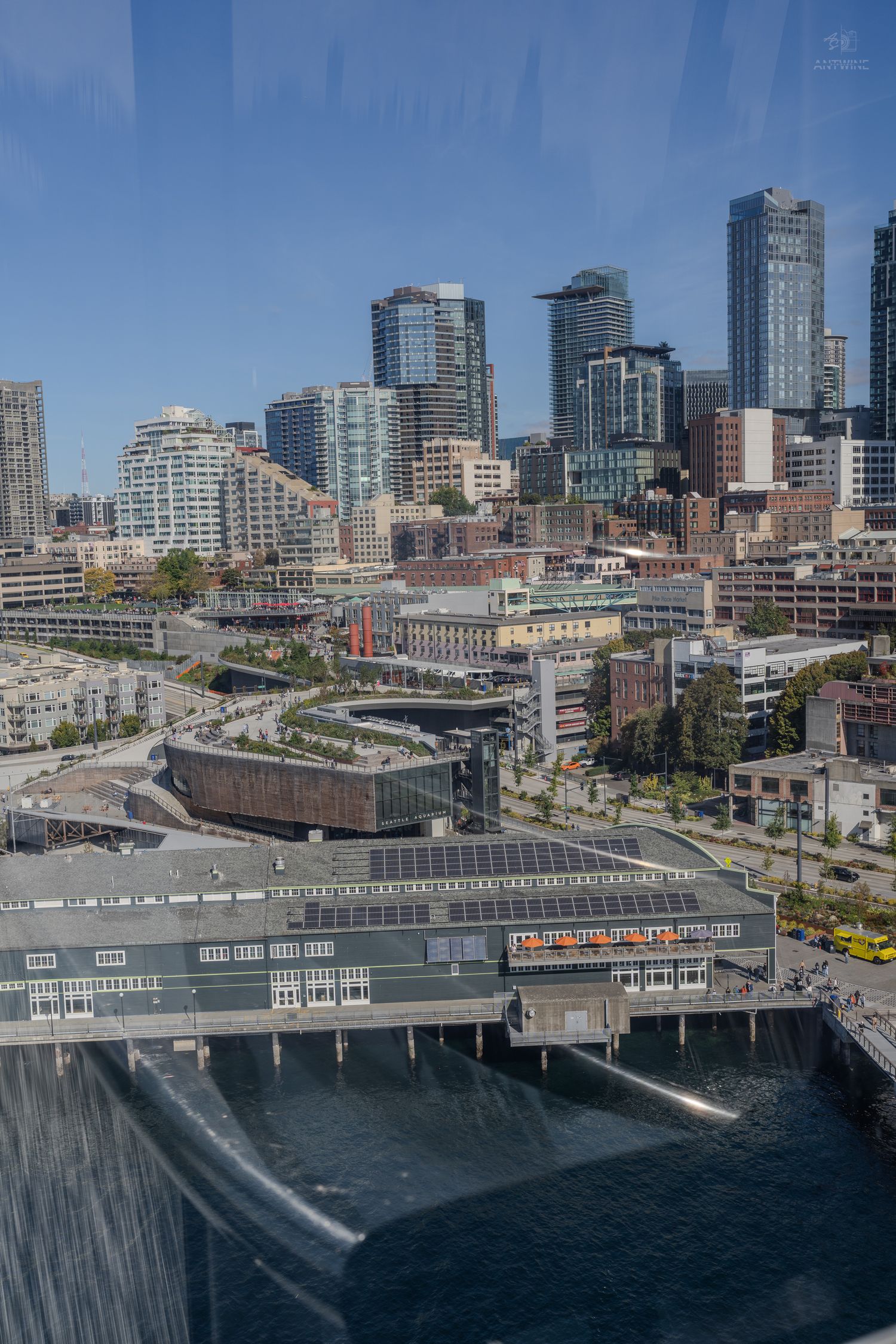 Aerial view of Seattle waterfront and downtown skyline with solar panel rooftop and Puget Sound visible.
