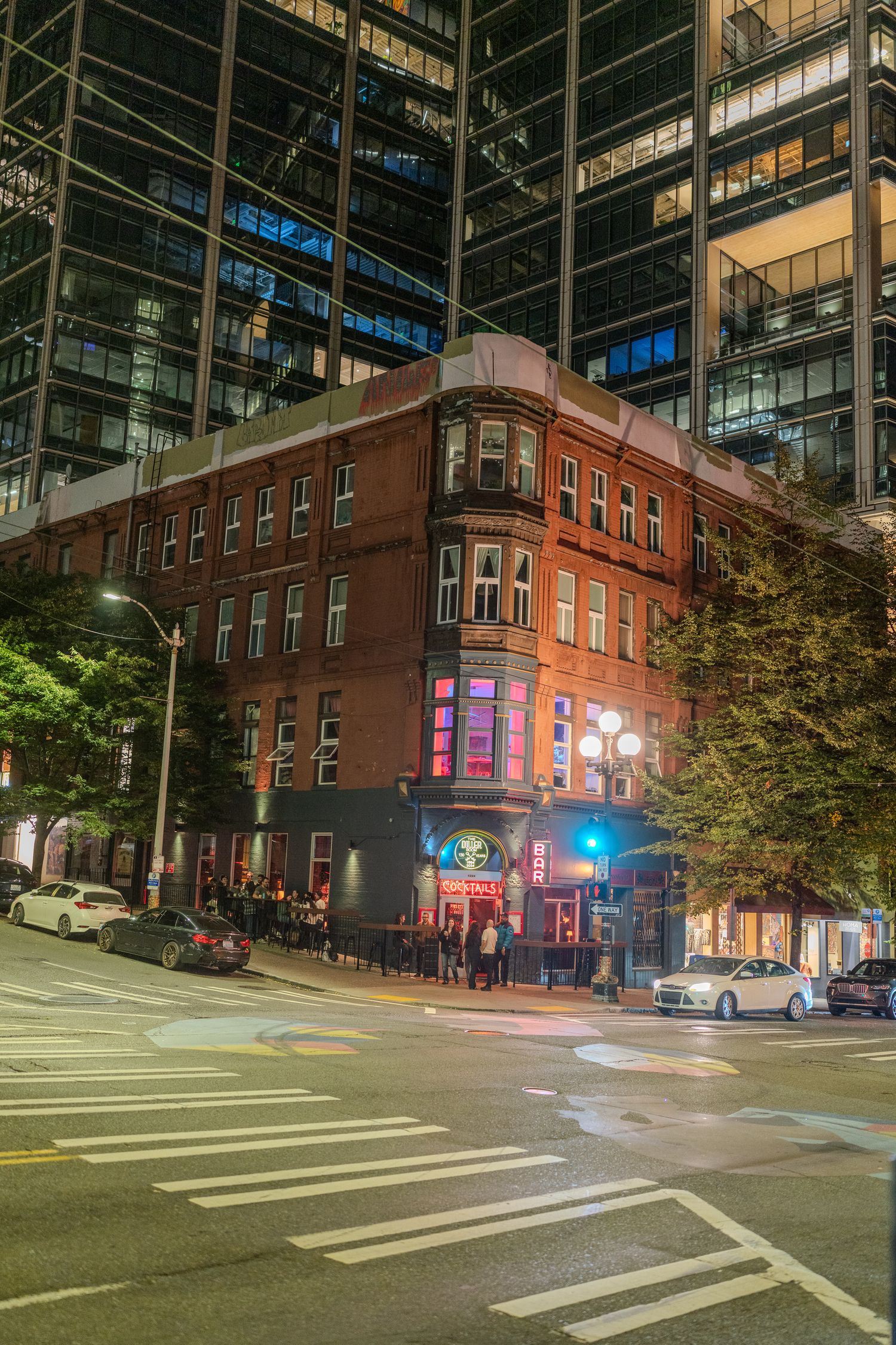 Historic red brick corner building with neon signs at night contrasting modern glass skyscraper in Seattle.